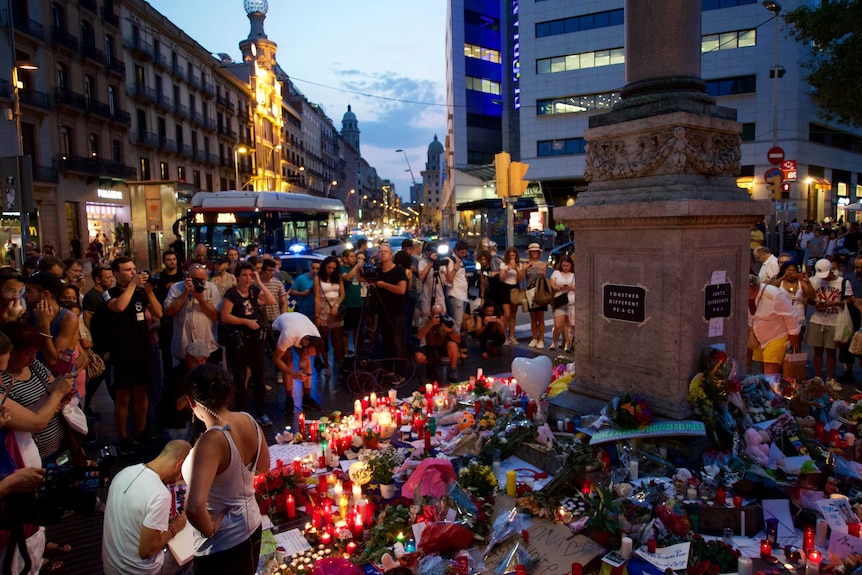 a growing floral and toy tribute surrounded by onlookers in central Barcelona