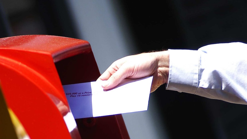 A man puts a letter in an Australia Post post box.