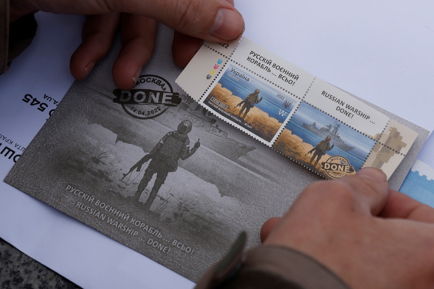 A man pastes a commemorative Snake Island stamps on a postcard