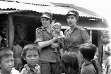 A black and white photograph showing two Australian nurses surrounded by Vietnamese children