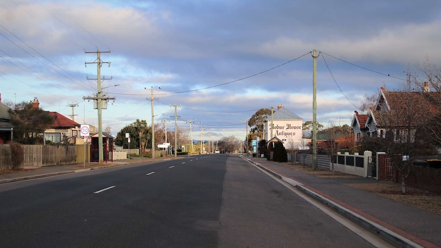 An empty main street in a small regional town lined with houses and an antiques store in the distance.