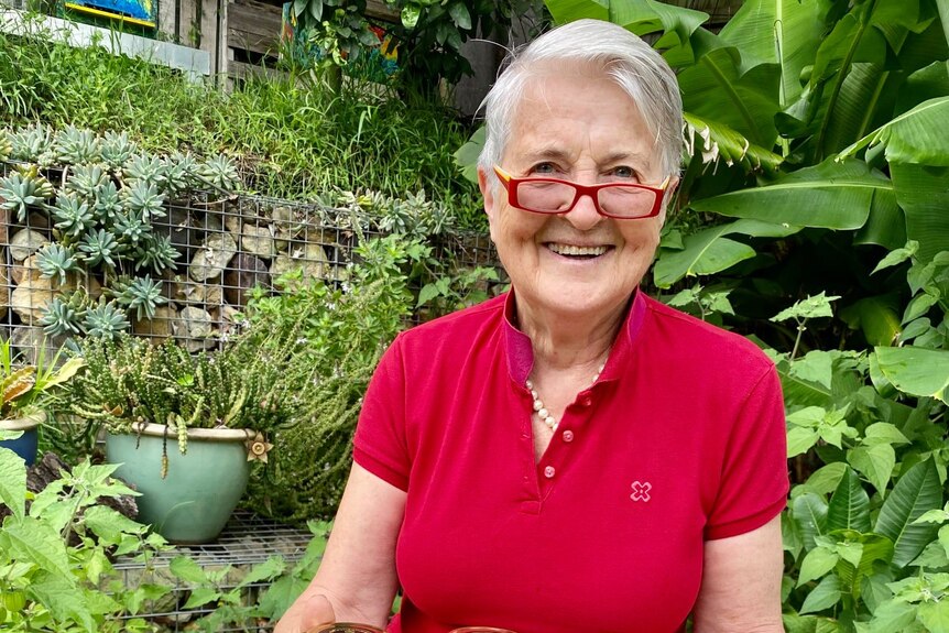 A woman in a red shirt with red glasses in a garden.