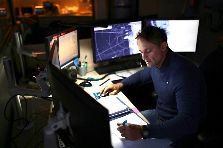 A Fremantle Port Authority Vessel Traffic Service Officer works in front of busy screens at night.