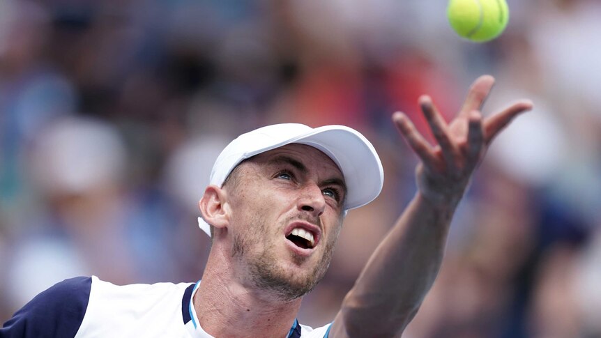 John Millman throws the ball in the air and stares at it intently.