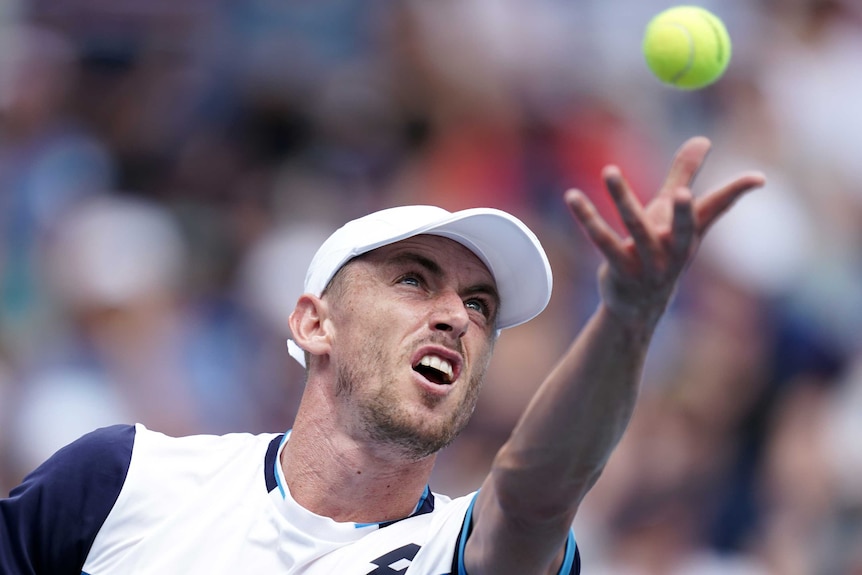 John Millman throws the ball in the air and stares at it intently.