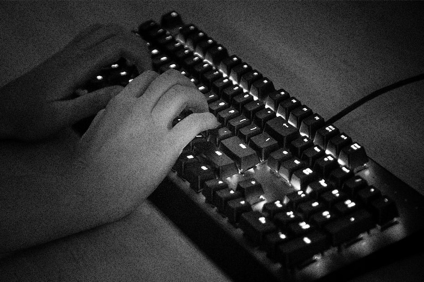 Black and white photo of two hands on a computer keyboard. The keys are backlit.