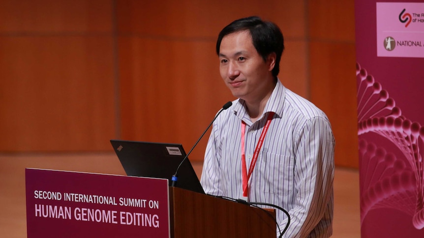 Scientist He Jiankui stands behind a podium with "SECOND INTERNATIONAL SUMMIT ON HUMAN GENOME EDITING" written on it.