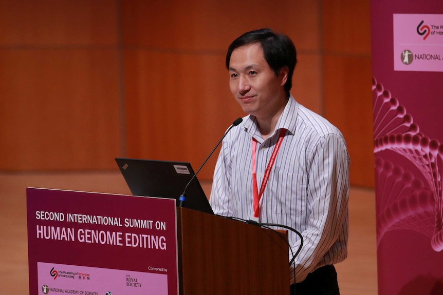 Scientist He Jiankui stands behind a podium with "SECOND INTERNATIONAL SUMMIT ON HUMAN GENOME EDITING" written on it.