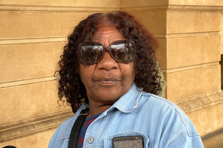 An Aboriginal woman wearing sunglasses outside a stone building