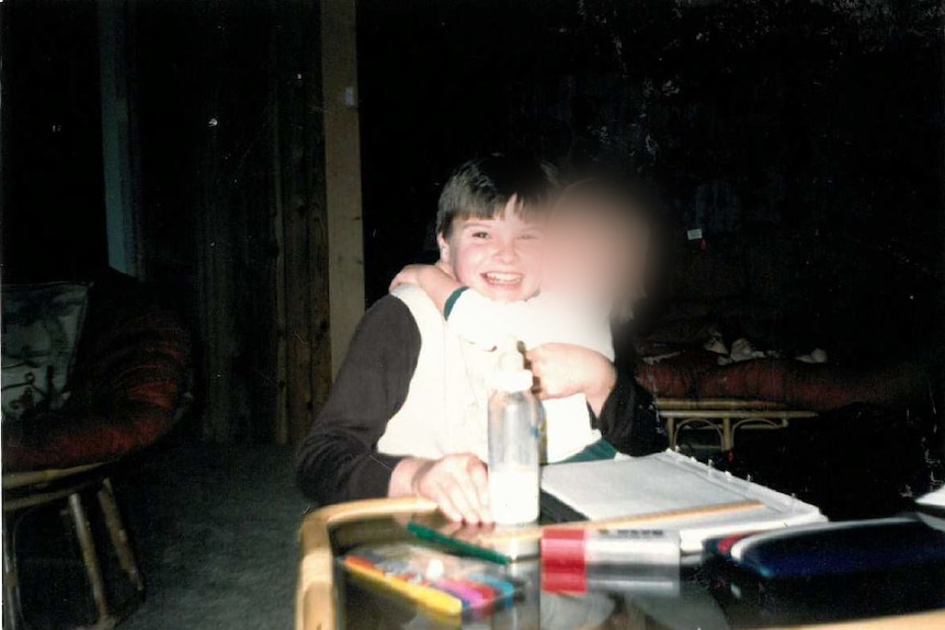 A smiling young boy cuddling a toddler sitting on his lap.