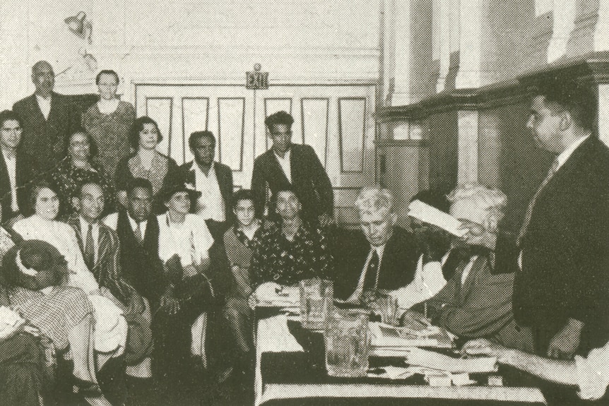 A black and white photo of 18 members of the Aborigines' Progressive Association at a meeting in a Sydney hall.