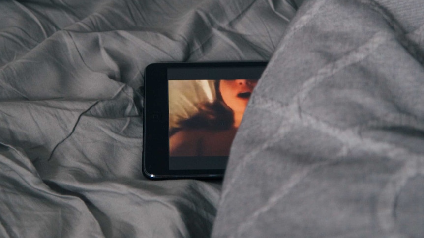 a phone displaying an intimate video, it is on a bed, with a bedsheet partially covering the image