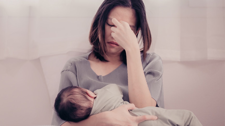 A woman sitting on the couch looking exhausted with her child for an article about postnatal depression and anxiety.