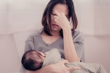 A woman sitting on the couch looking exhausted with her child for an article about postnatal depression and anxiety.