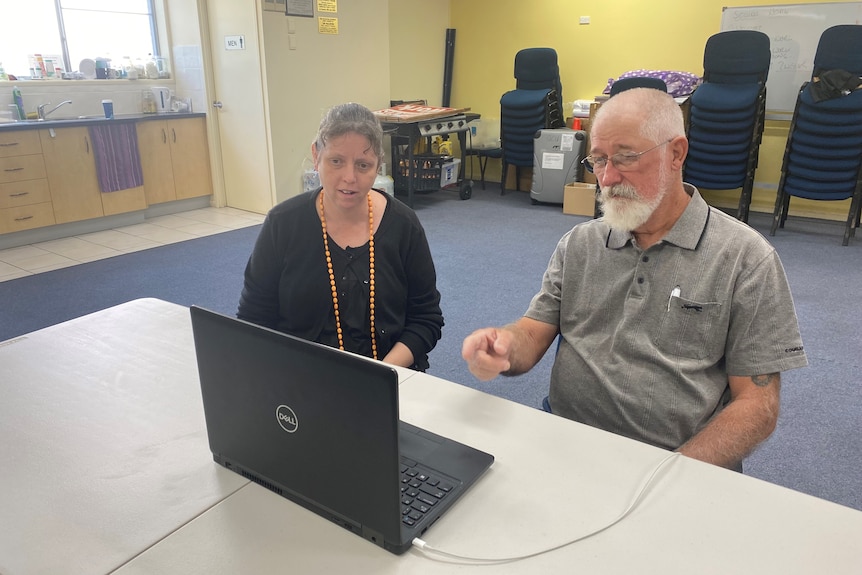 A young woman sits beside an older, bearded man at a laptop