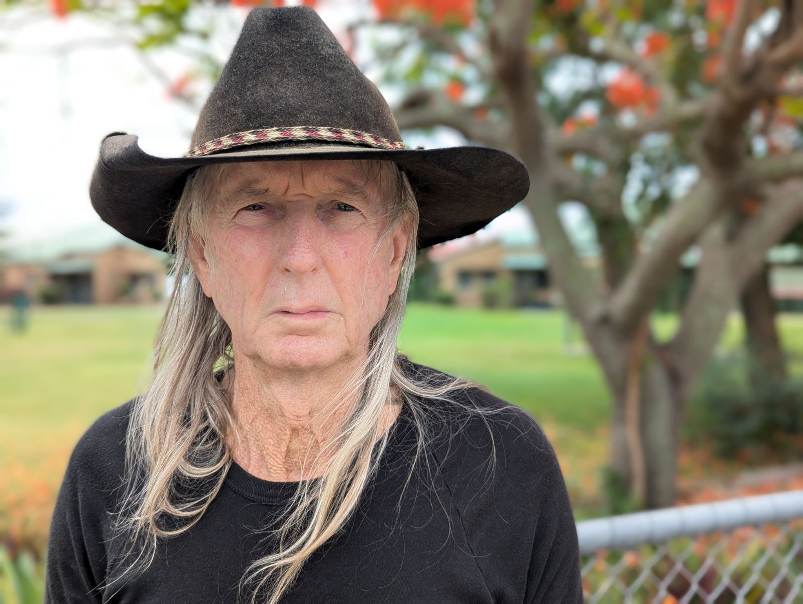 A serious-looking older man in a black shirt and large hat.