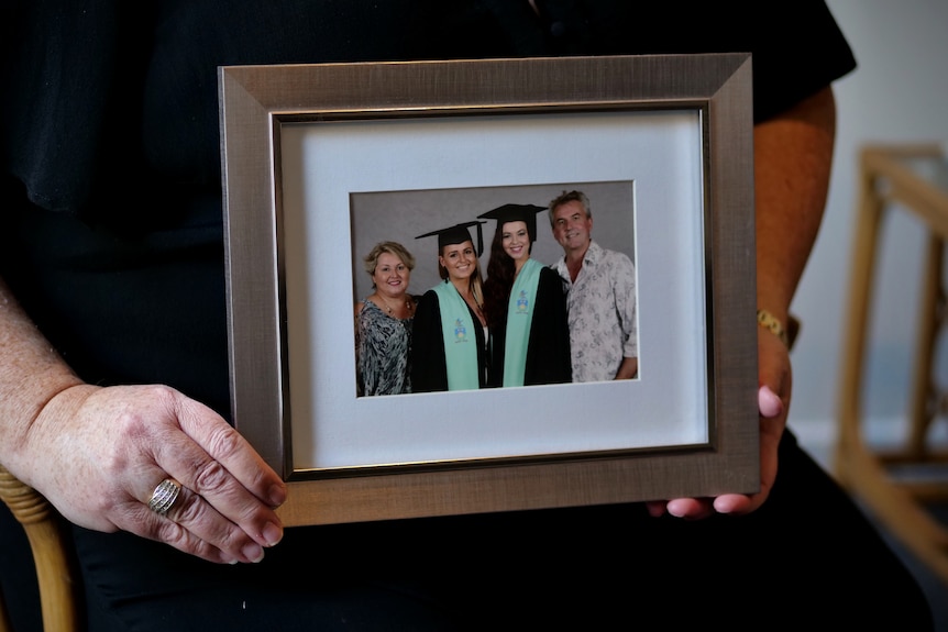 A close up of university graduation photo of two girls with mum and dad in photo, a womans hands is holding the frame