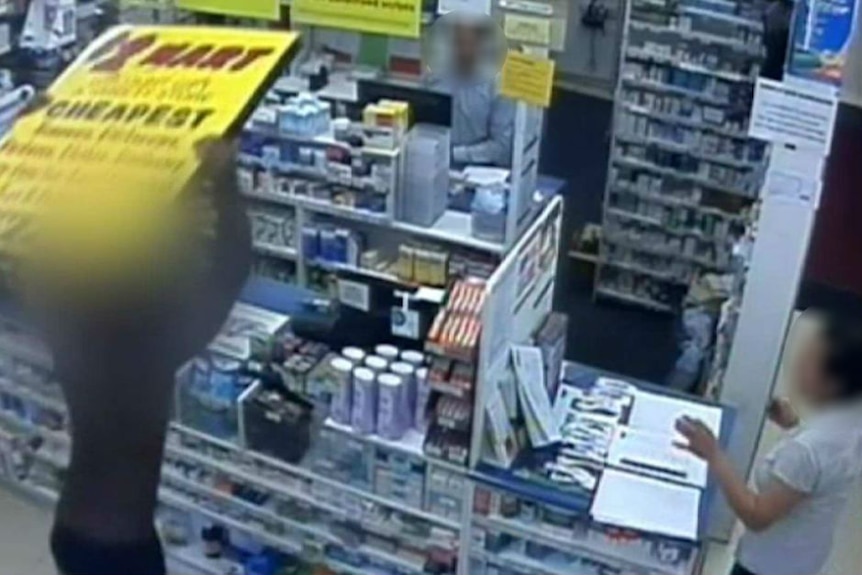 A man holds a sign over his head inside a chemist