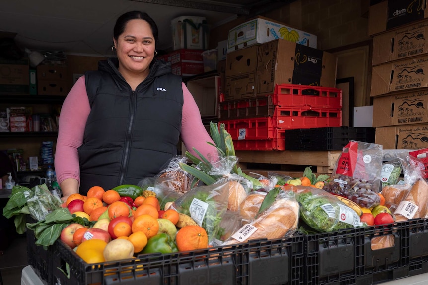 Smiling woman stands behind table of food hampers