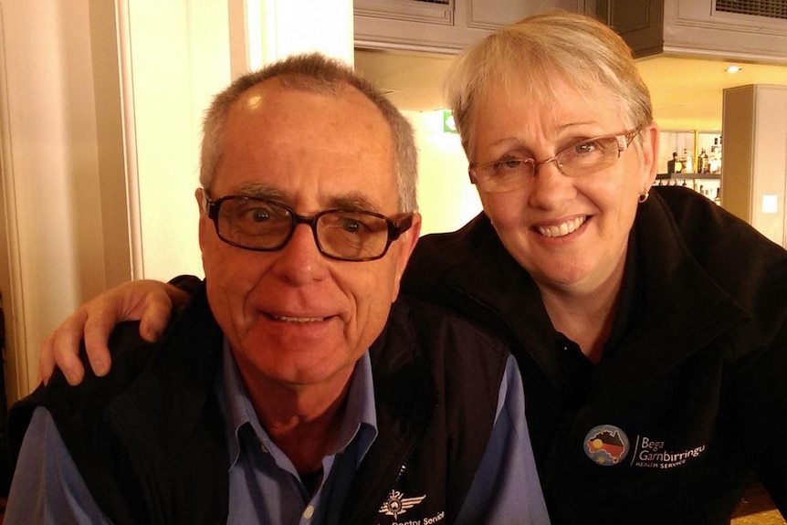 A man with glasses and a woman with short hair look towards the camera and smile.