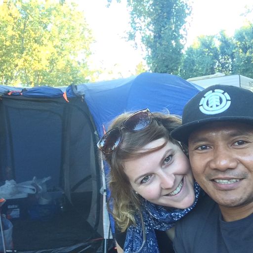 A couple smile for a selfie. There is a tent in the background.