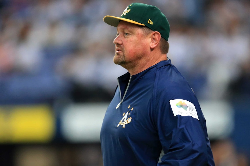 A cap-wearing baseball coach watches the play.