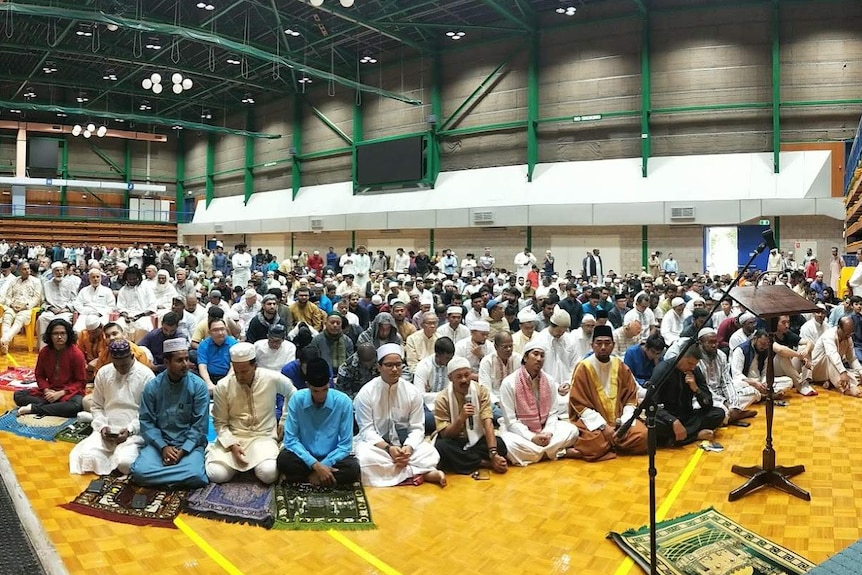 Muslim community sitting on floor praying.
