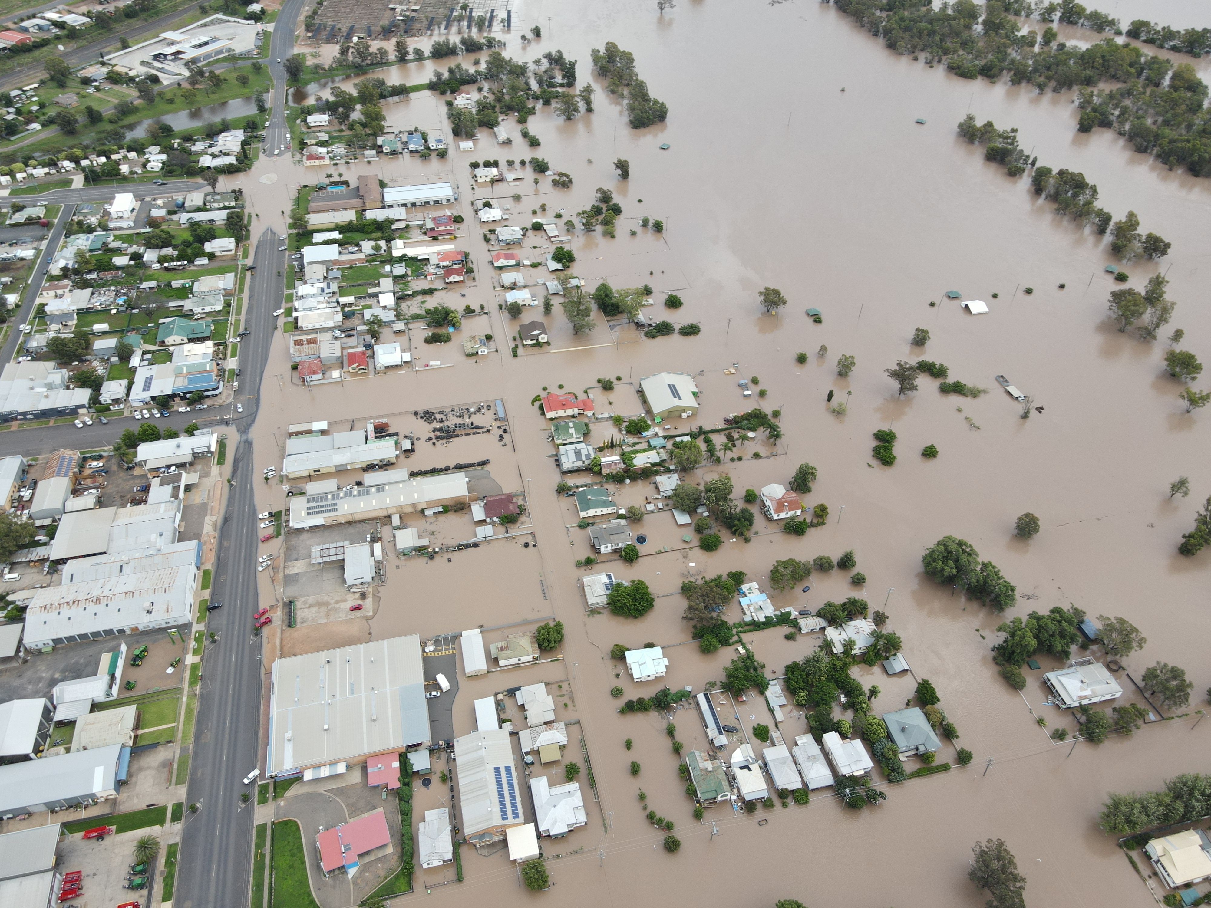 Houses and road inundated by brown floodwaters.