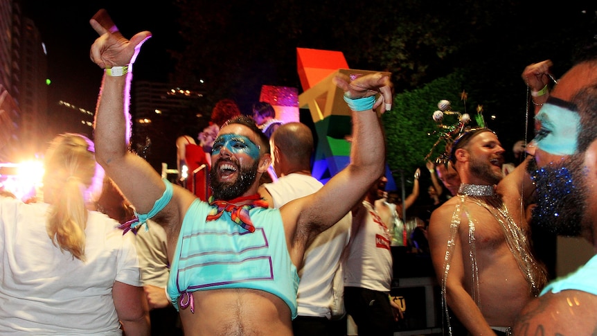 A man in a blue crop top and face paint celebrates during the Sydney Mardi Gras parade.