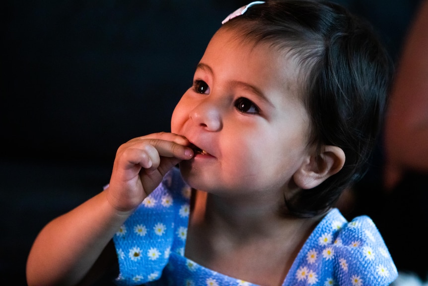 A toddler in a blue dress looks off into the distance 