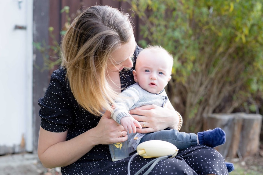 A woman expressing breast milk while holding her baby.