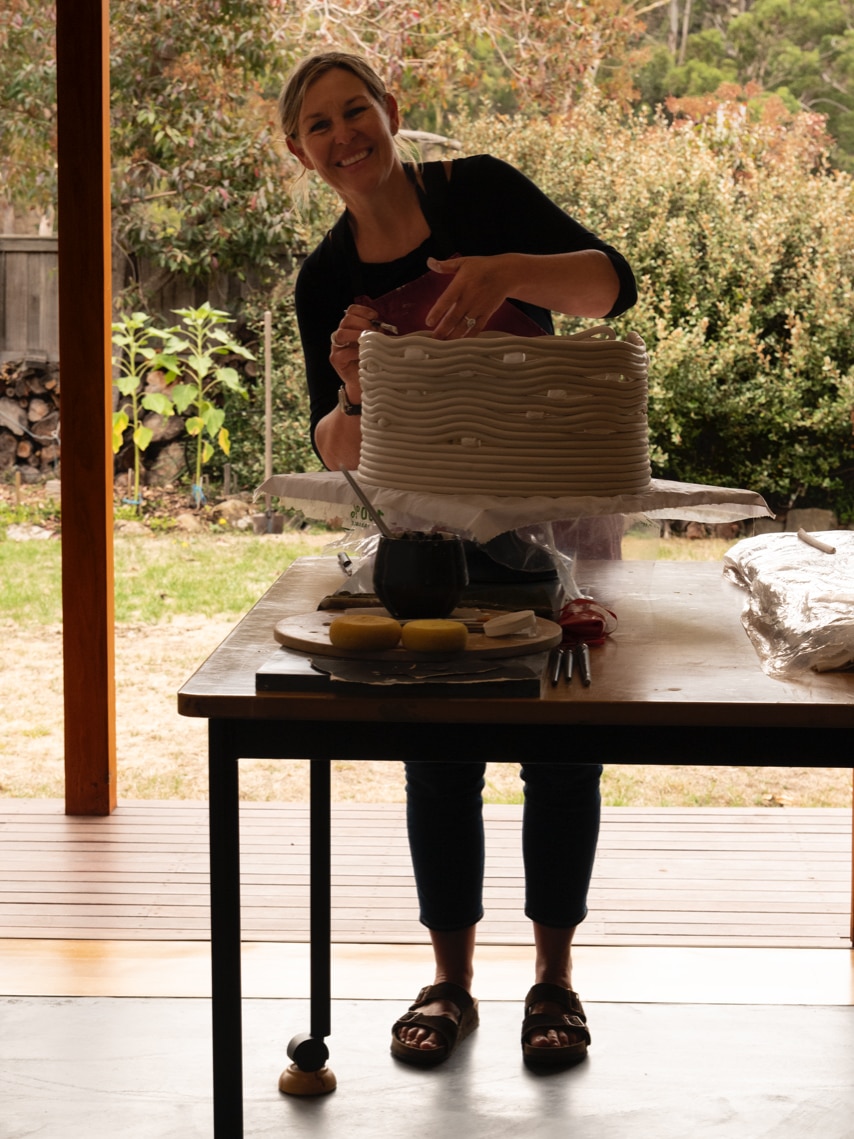 A woman working a clay piece of art, standing, smiling at the camera