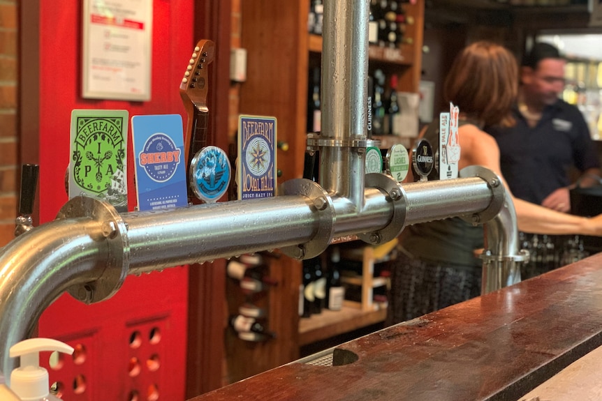 Beer taps in the foreground with people working behind a bar in the background