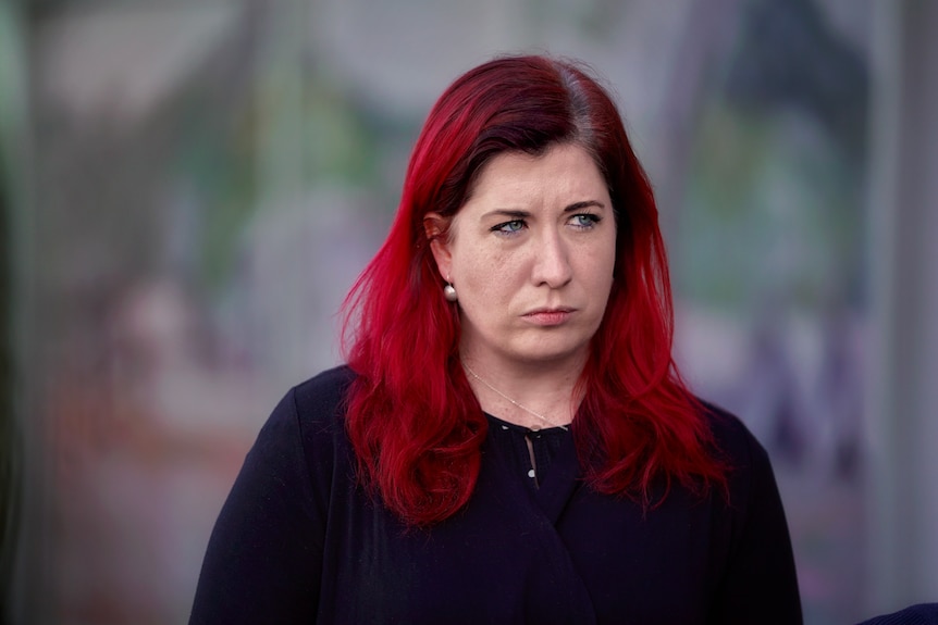 A woman with dyed red hair is frowning.