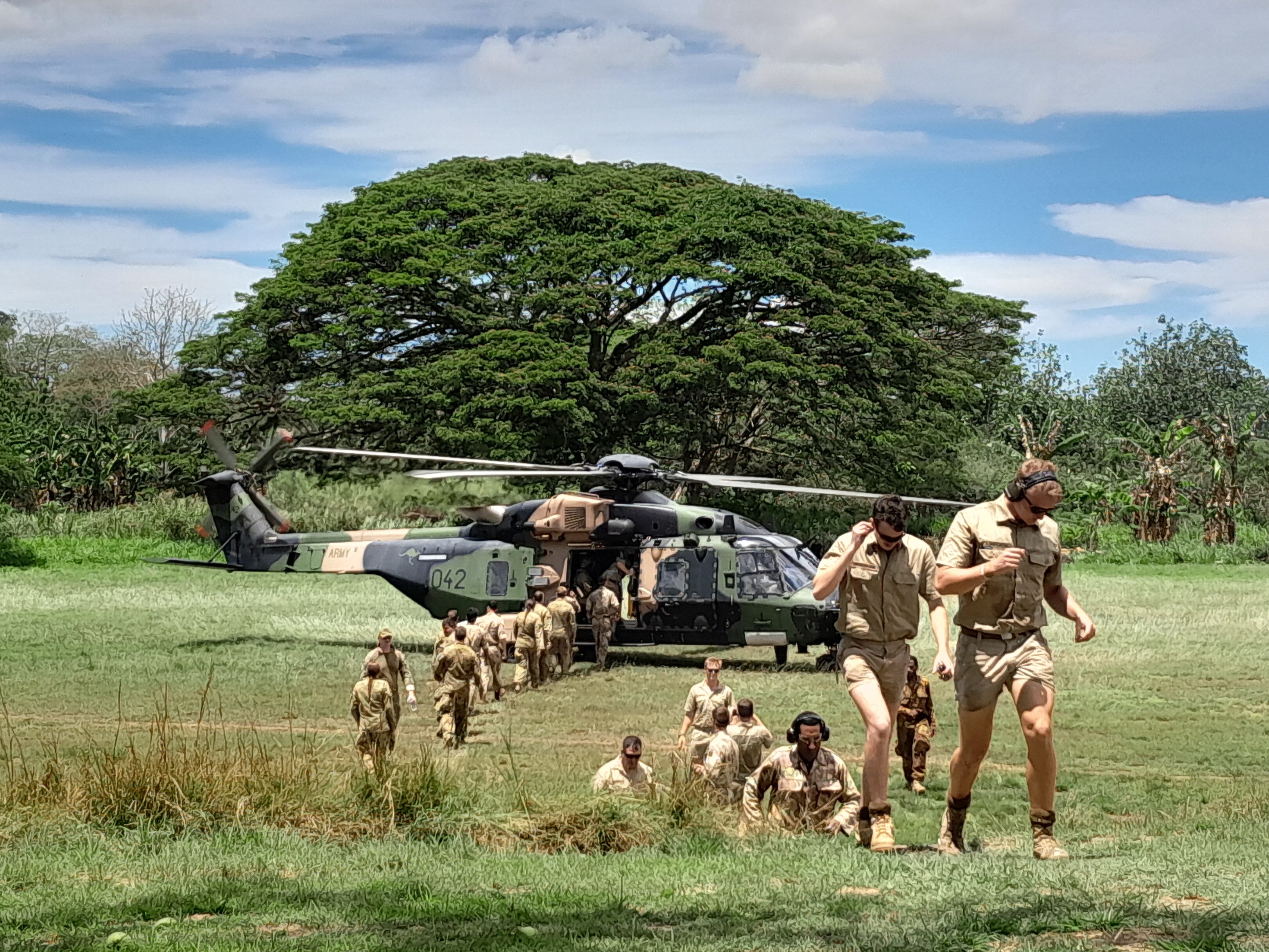 A line of soldiers leaves a helicopter grounded in a field.