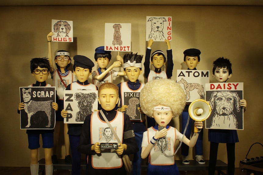 Colour still of student animal activists holding up posters of dogs in a protest in stop-motion animation Isle of Dogs.