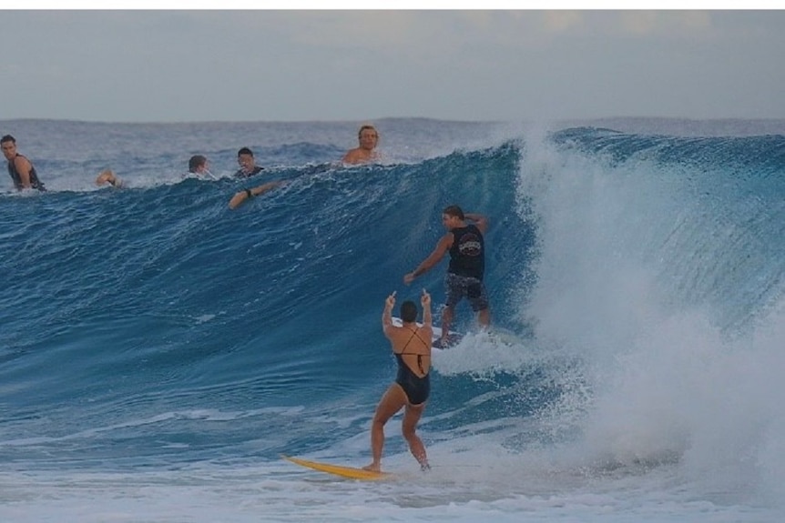 A woman surfer is riding her surfboard on a wave in the ocean and a male surfer is on the same wave.