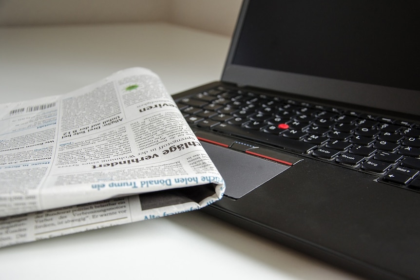 Folded newspaper and laptop with black screen