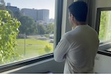 A man stands at a window looking outside.