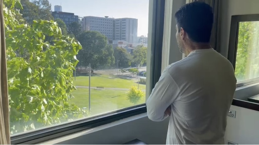 A man stands at a window looking outside.