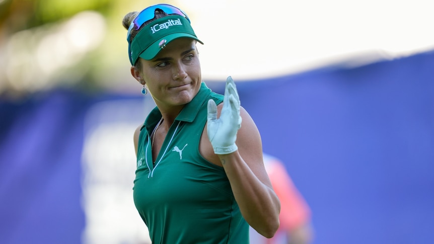 A golfer looks over her shoulder and raises a hand to the crowd after holing a putt at a major tournament.