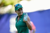A golfer looks over her shoulder and raises a hand to the crowd after holing a putt at a major tournament.