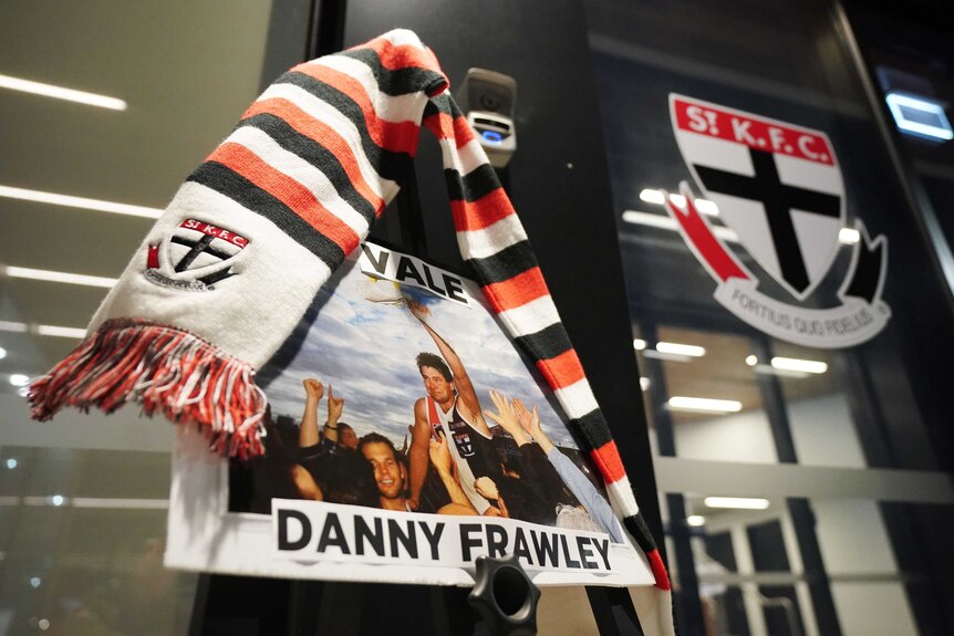 A picture with the words "Vale Danny Frawley" is placed on a door with a St Kilda scarf on it.