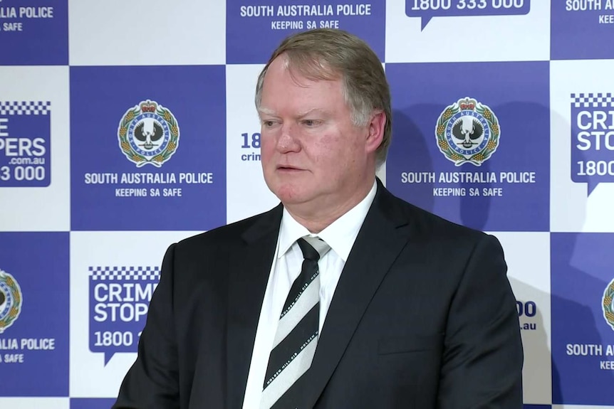 A man wearing a black suit in front of a police backdrop