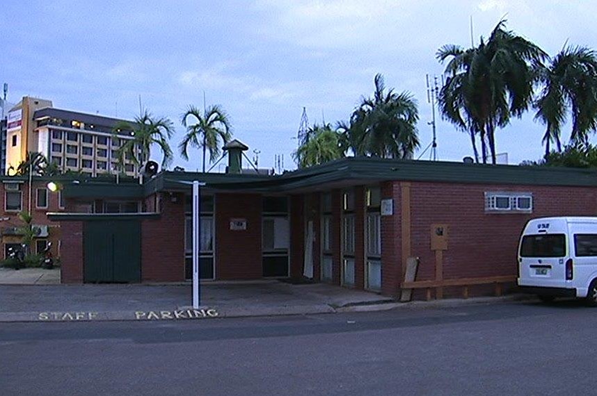 The Palms motel is seen from the back. The brick building has green accents and palm trees are seen above.