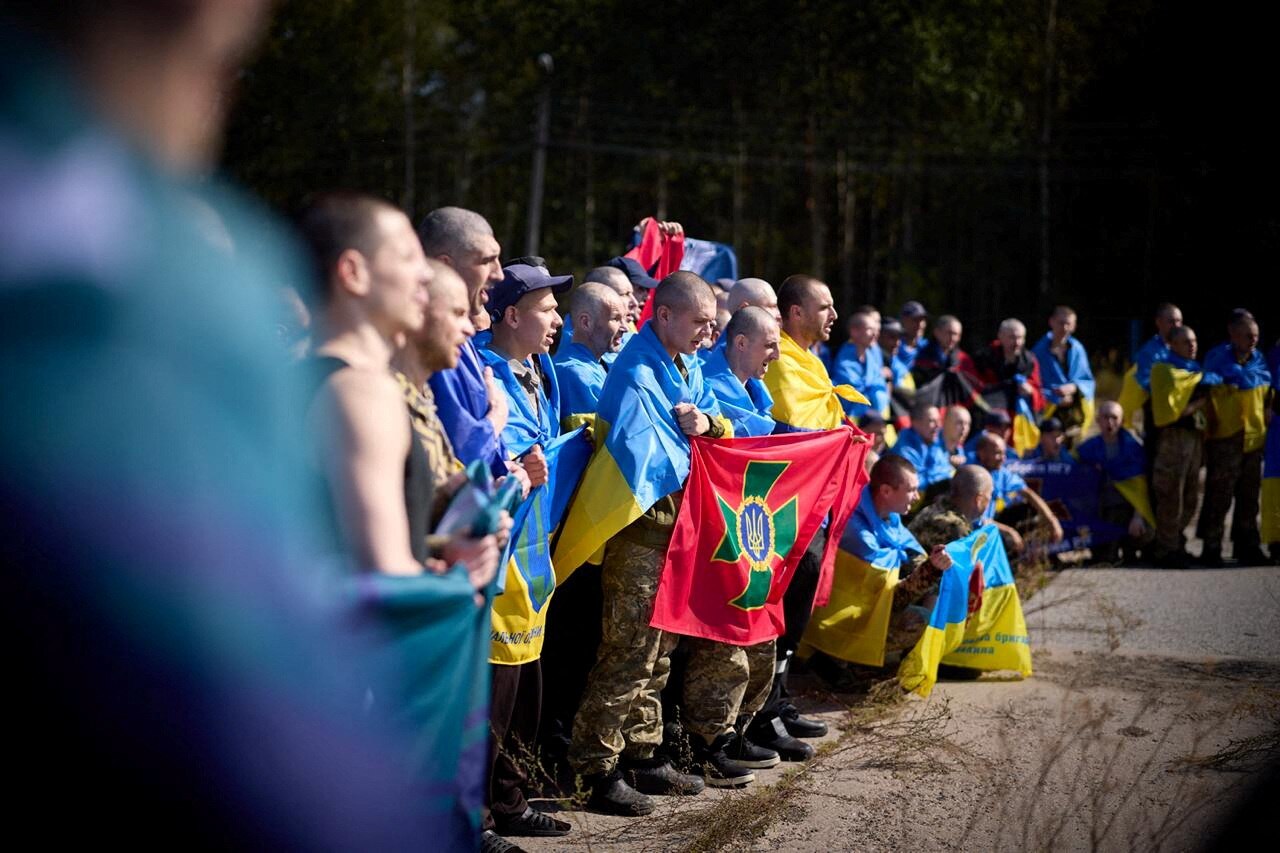 Rows of people wearing the Ukraine flag around their necks and backs, seen from one side.