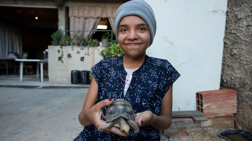 A teenaged girl in a beanie holding a turtle