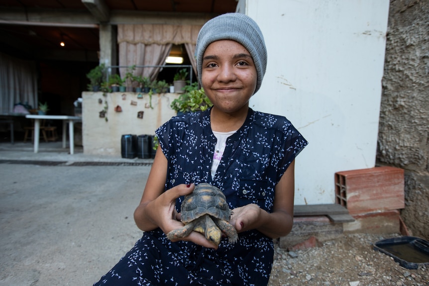 A teenaged girl in a beanie holding a turtle