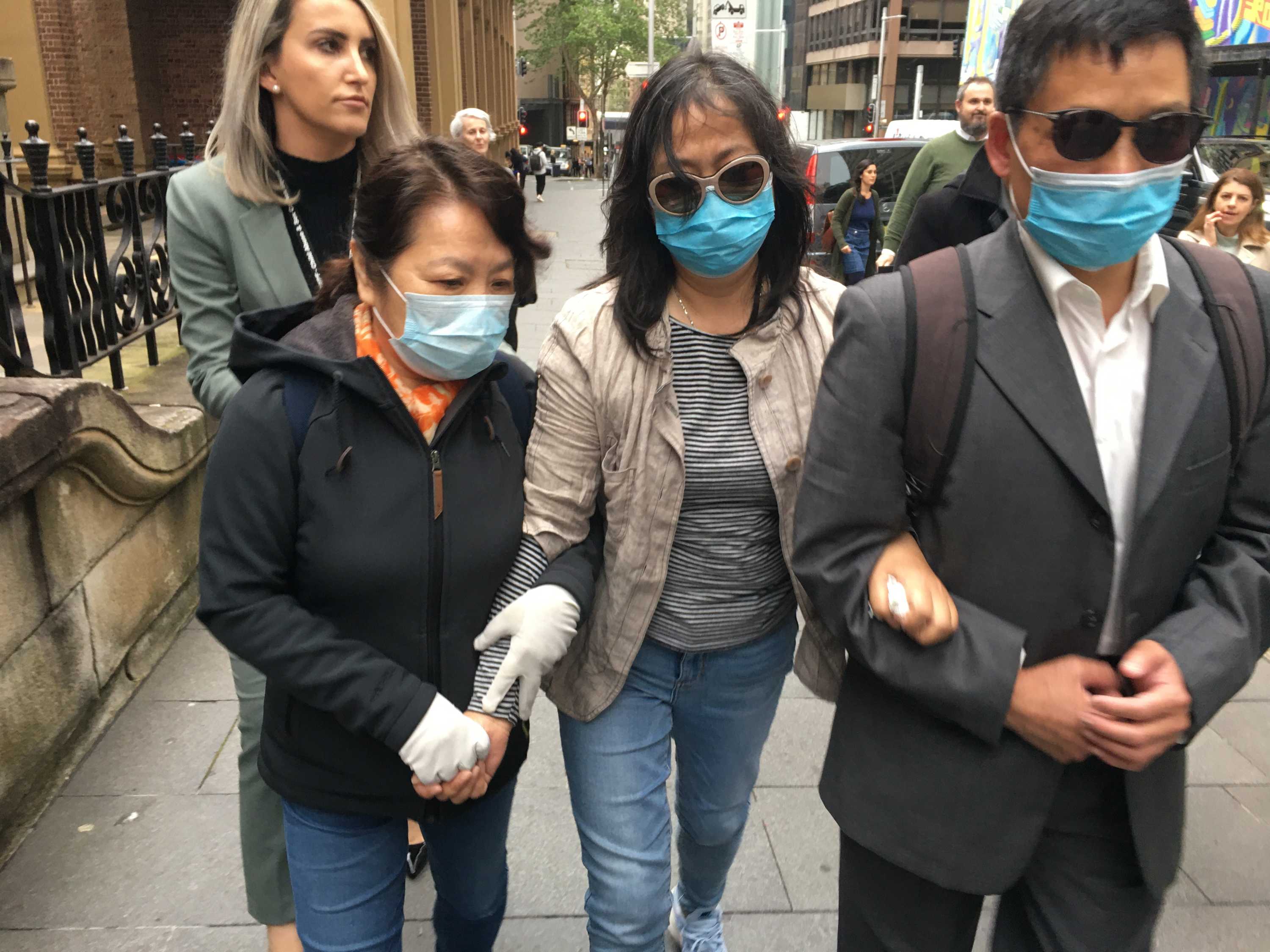 Three Chinese people wearing masks walk with arms linked.