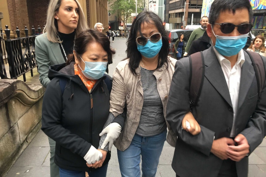 Three Chinese people wearing masks walk with arms linked.